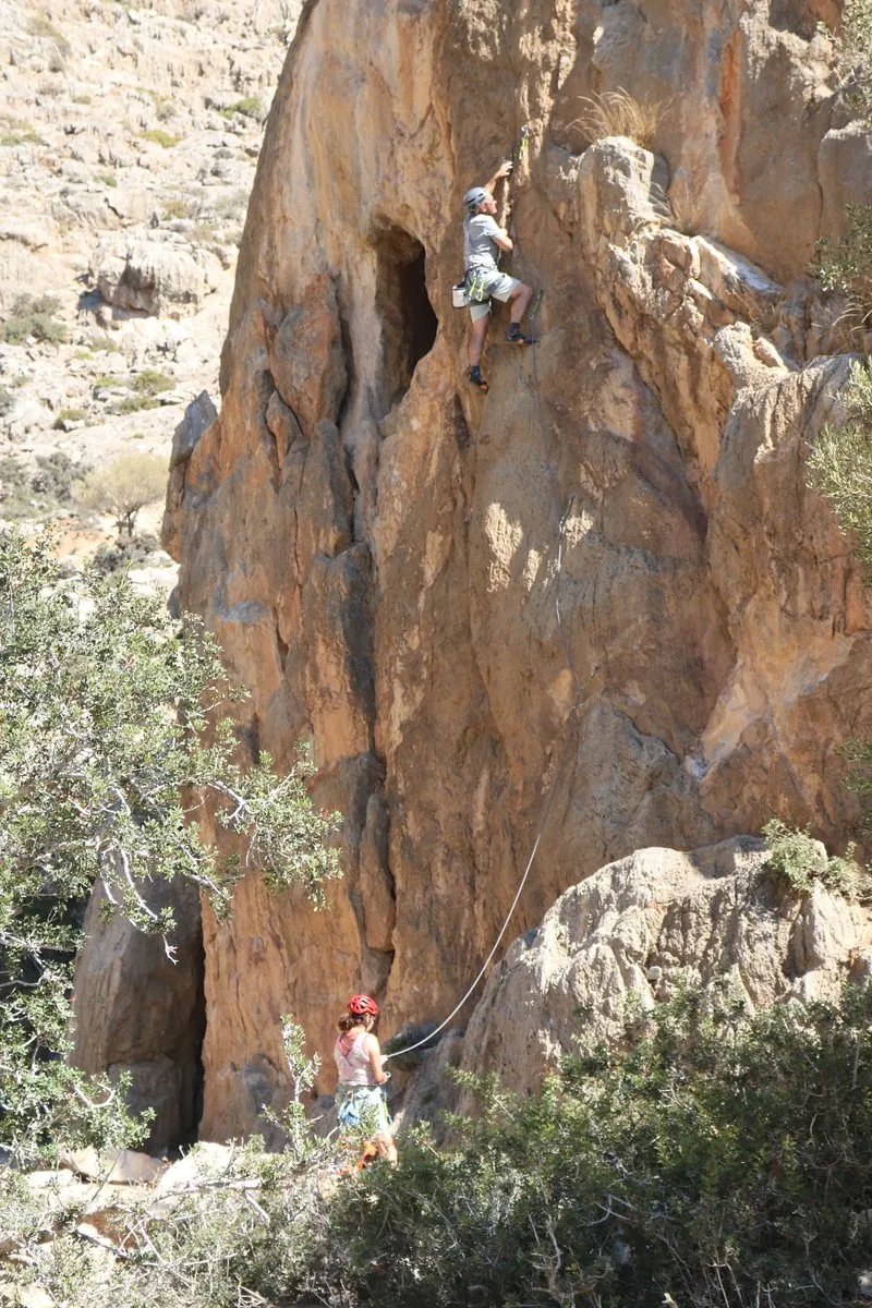 A climber high on a rock tower in the Agiofarango gorge, belayed from below