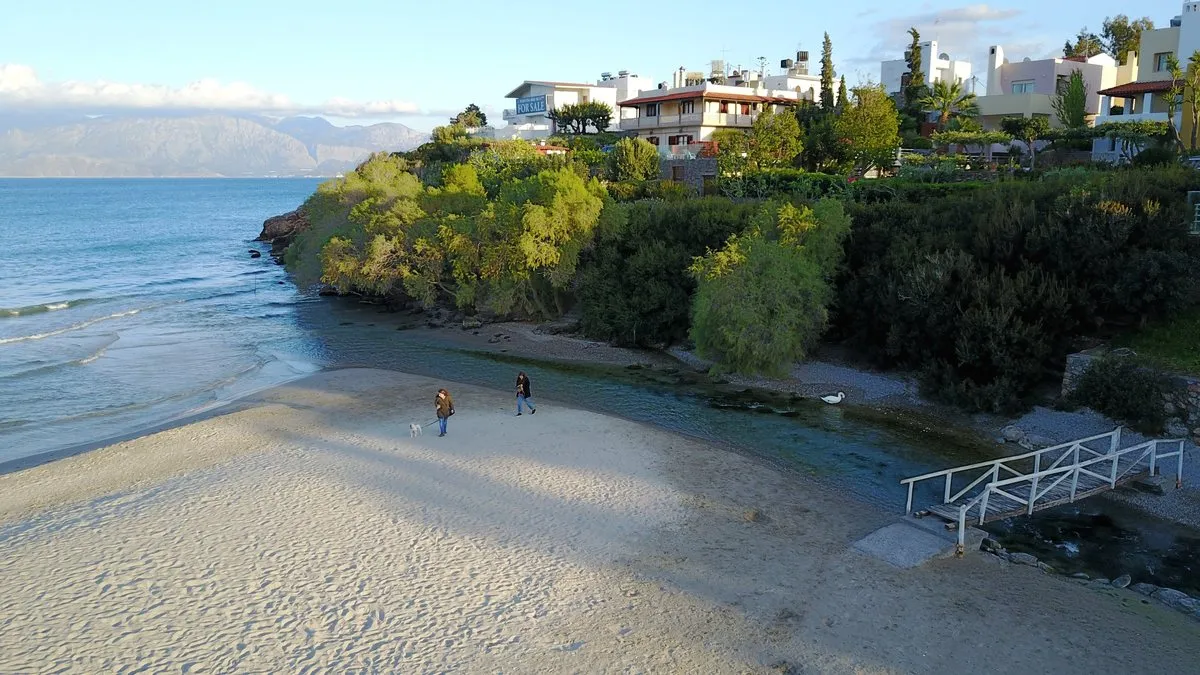 Der Sand am Strand von Almyros, darüber Gärten und Häuser am Hang