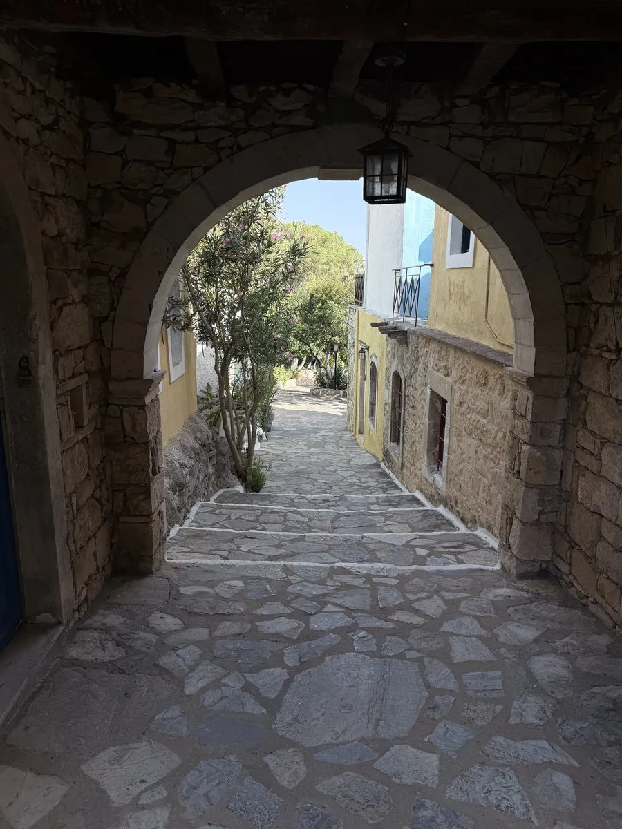 A stone arch over a stepped lane at Arolithos, with a lantern and a whitewashed house beyond