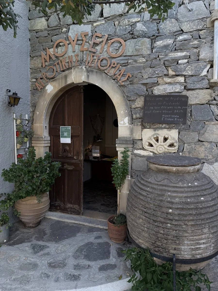 The arched stone entrance of the Museum of Rural History and Folk Craft at Arolithos, with a large jar beside the door