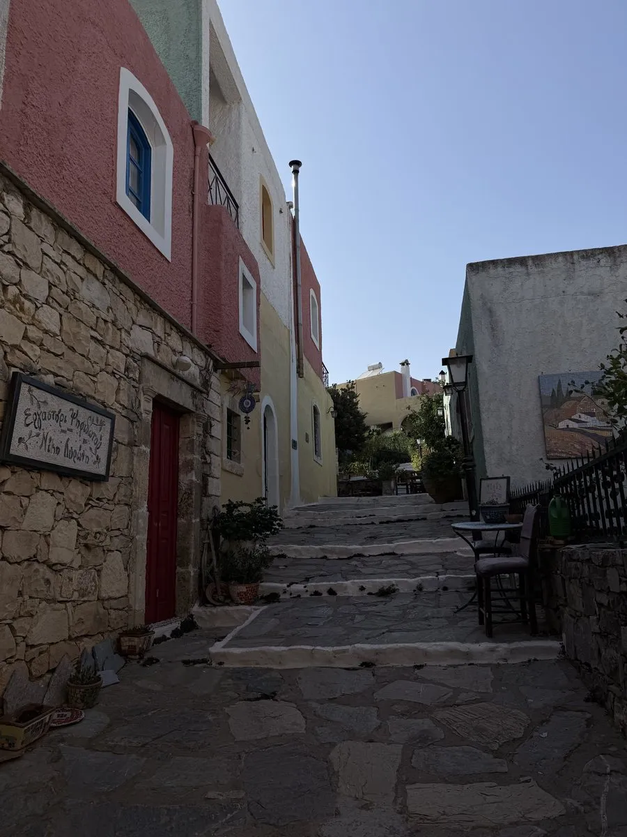 Houses in rose, ochre and sage green along a stepped lane at Arolithos