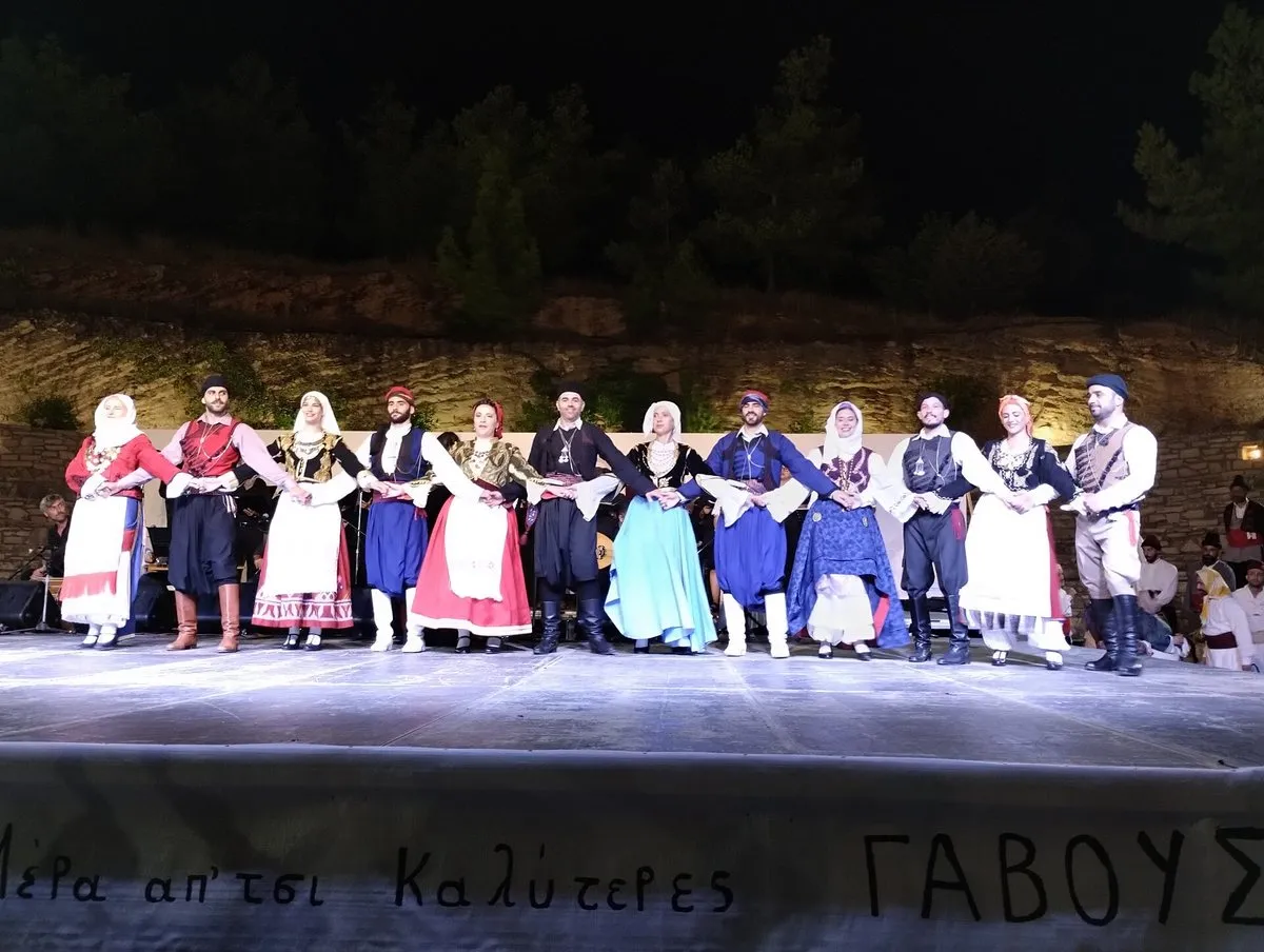 A line of dancers in traditional Cretan costume on a lit stage at the Gavoustima festival in Sitia