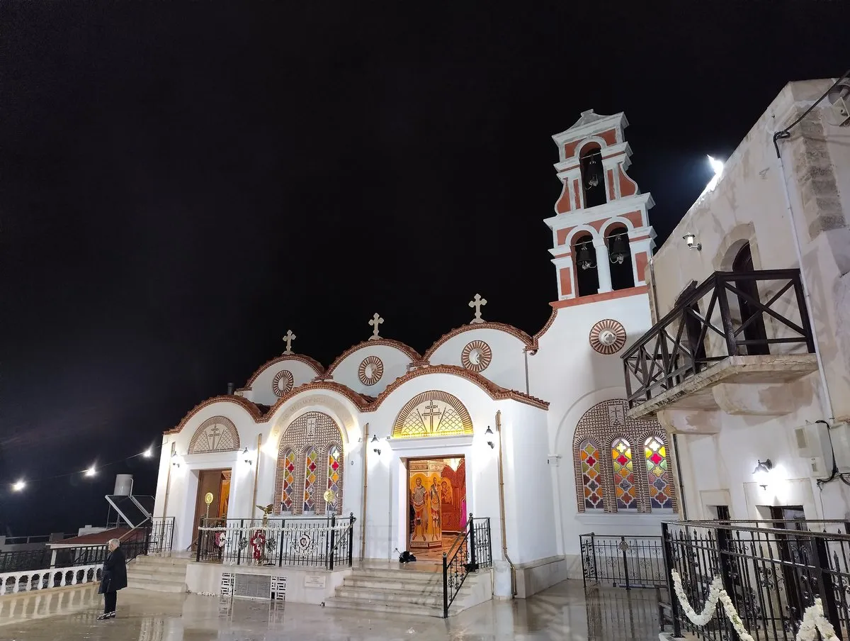 A village church lit up at night on Easter Saturday, people gathered on the steps