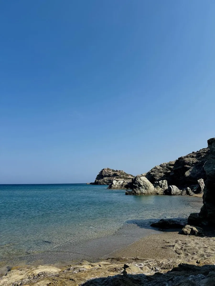 Shallow clear water at Erimoupolis with rock in the foreground and the ruined headland of Itanos beyond