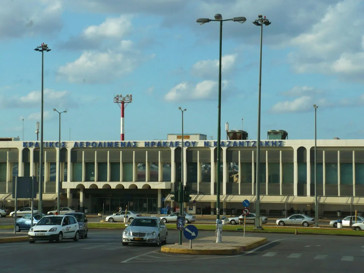 Das Terminalgebäude des Flughafens Heraklion vom Vorplatz, davor Autos und Straßenlaternen