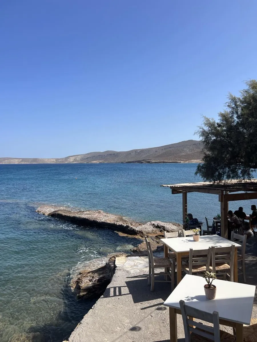 Taverna tables on the rocks at the water at Hiona beach, with the bay and bare hills behind