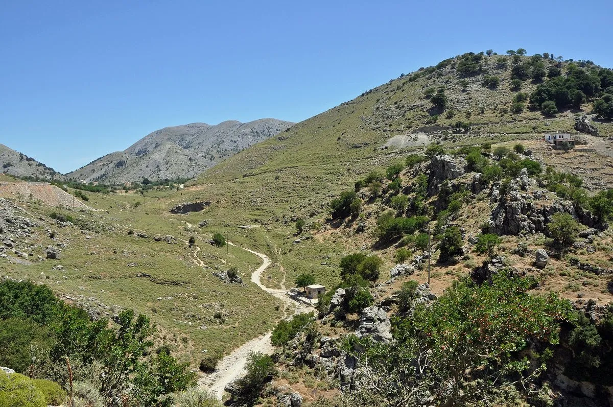 The upper part of Imbros Gorge, a stony path winding down a wide green valley between bare limestone ridges