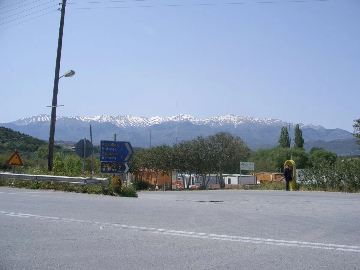 The view from the bus stop at Kalyves, road signs at a junction with the snow-topped White Mountains behind