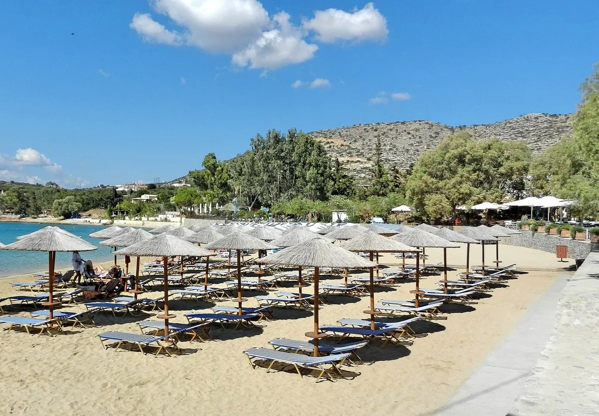 Liegen und Sonnenschirme auf dem Sand von Marathi, dahinter die Hügel der Souda-Bucht