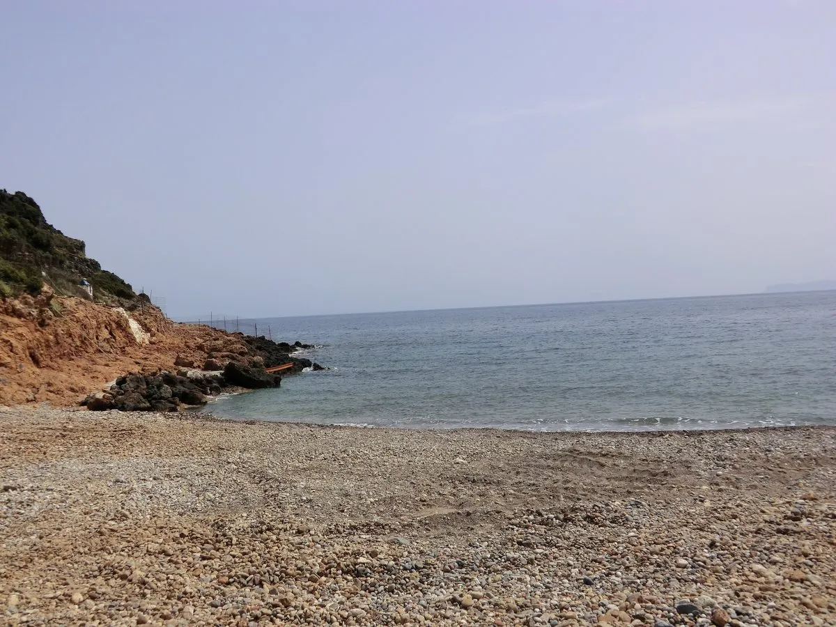 Ein Kiesstrand in Kolymbari mit einer Landspitze aus rotem Fels