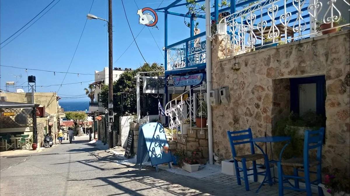Eine Gasse in Koutouloufari mit Tavernentischen und dem Meer am Ende