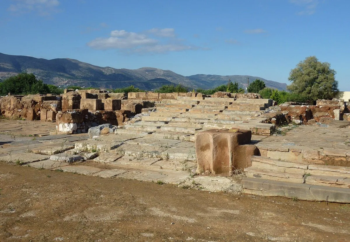 The grand staircase at the Palace of Malia, wide shallow stone steps leading up from the excavated court with mountains behind