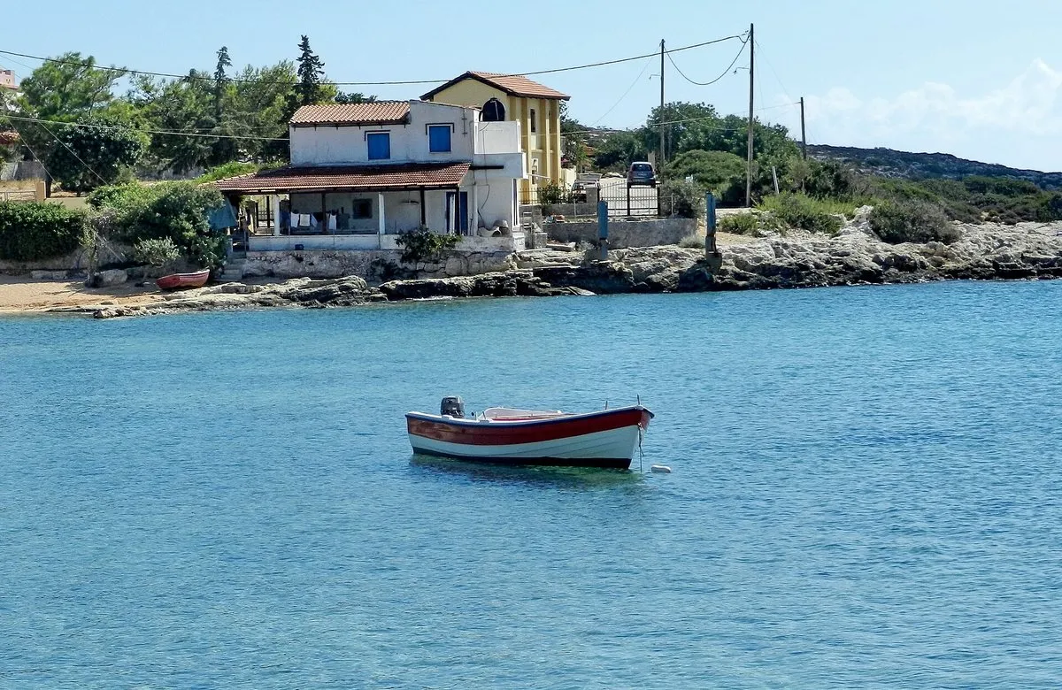 Ein kleines Fischerboot im ruhigen Wasser einer Bucht in Marathi, Häuser am Ufer