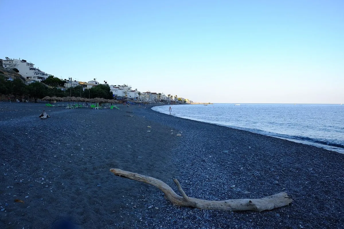 The dark-sand beach curving away at dusk