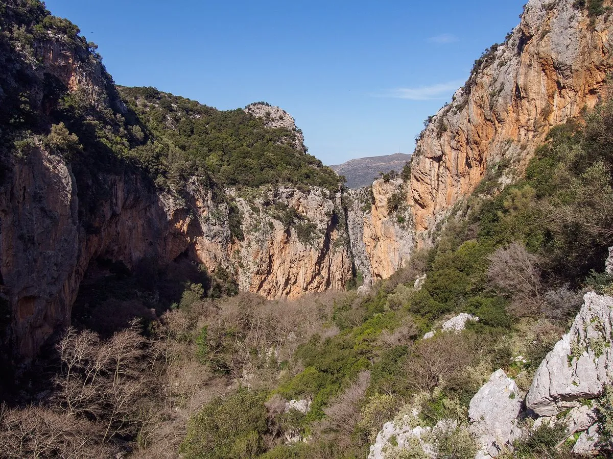 Hohe orangefarbene Felswände über dem grünen Grund der Patsos-Schlucht