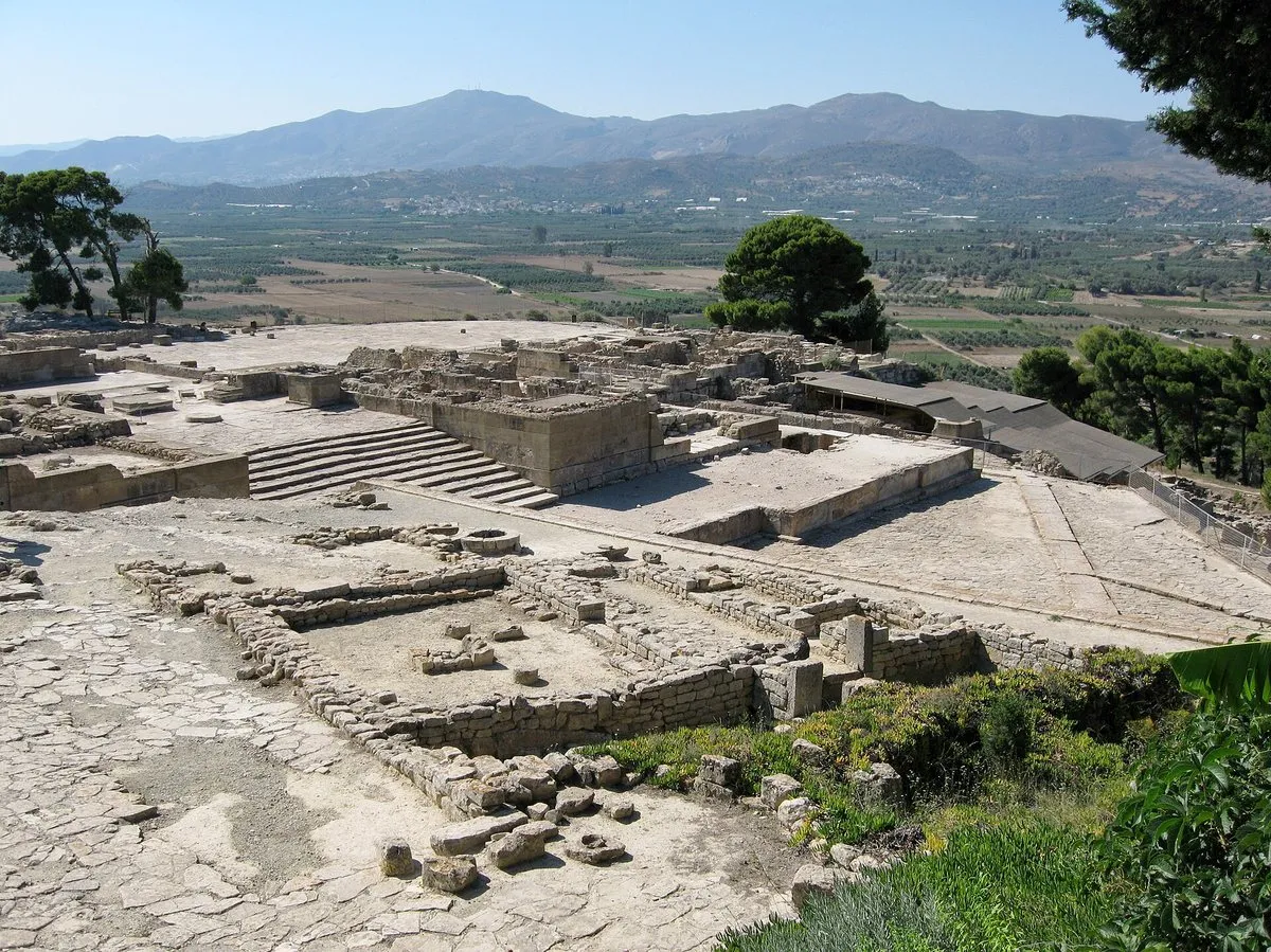 The excavated terraces and wide stone staircase at Phaistos, low walls spreading across the ridge with olive groves beyond