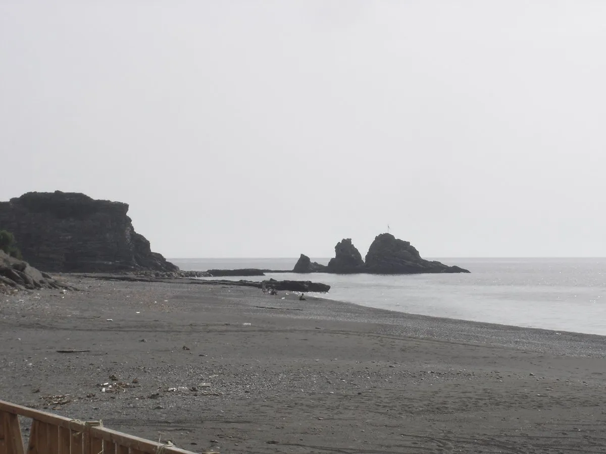 Der dunkelgraue Sand des Strandes von Sidonia, mit Felsen im Meer am hinteren Ende
