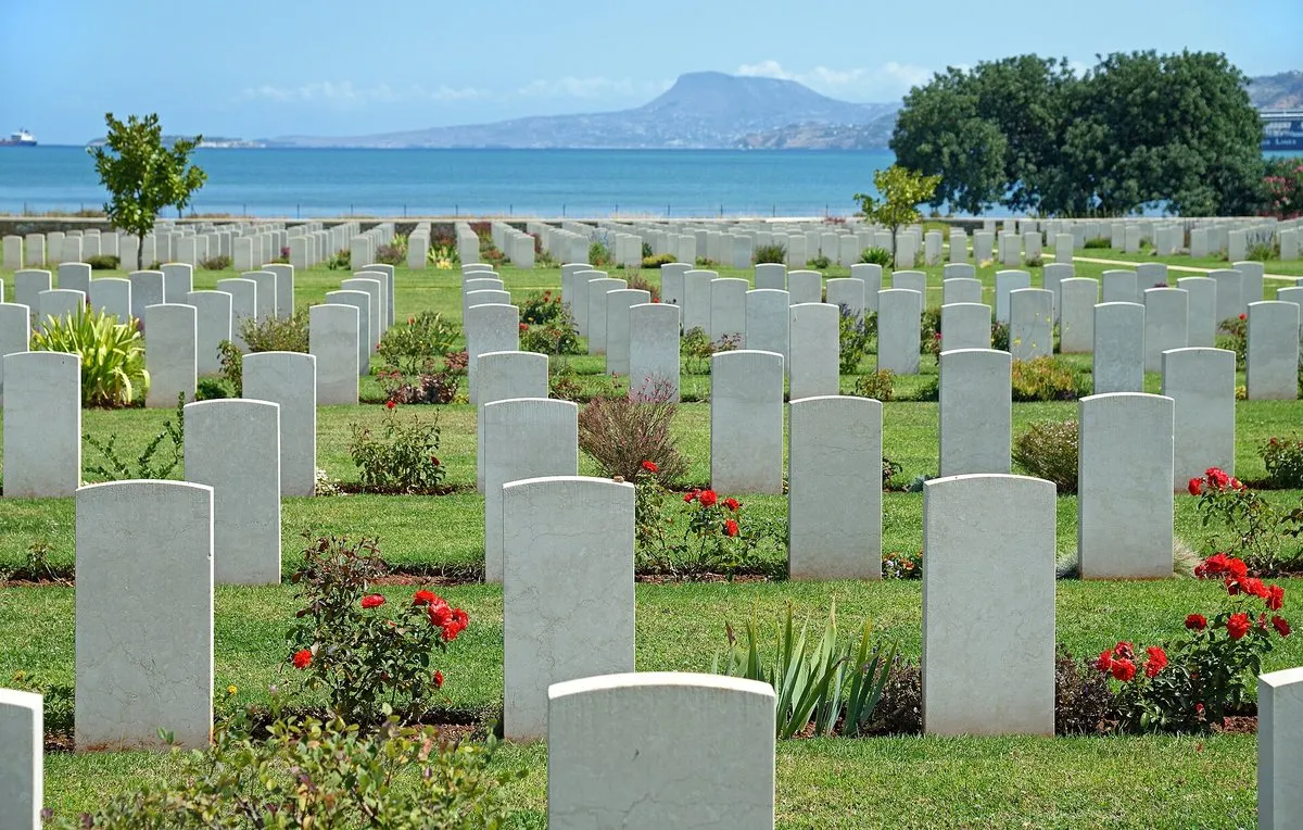 Rows of white headstones at the Souda Bay Allied War Cemetery with the bay behind