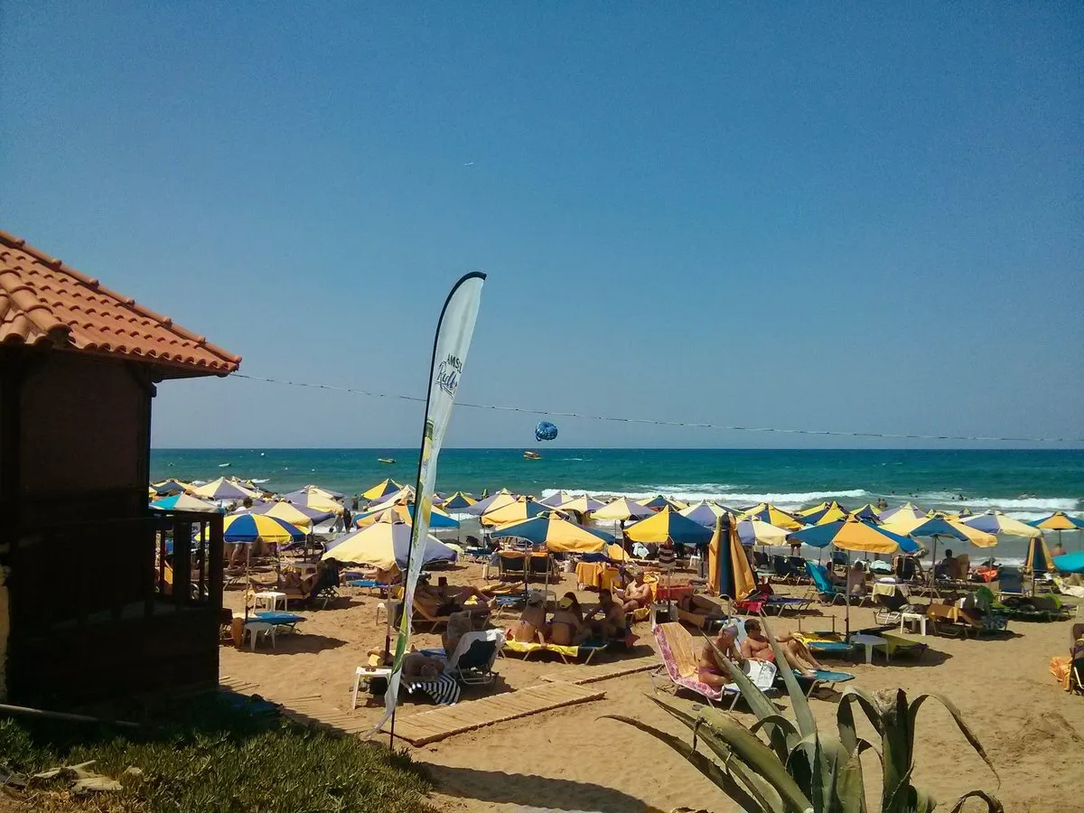 Reihen von Sonnenschirmen und Liegen am Sandstrand von Stalis